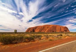 a road leading to a large rock formation in the middle of a desert .