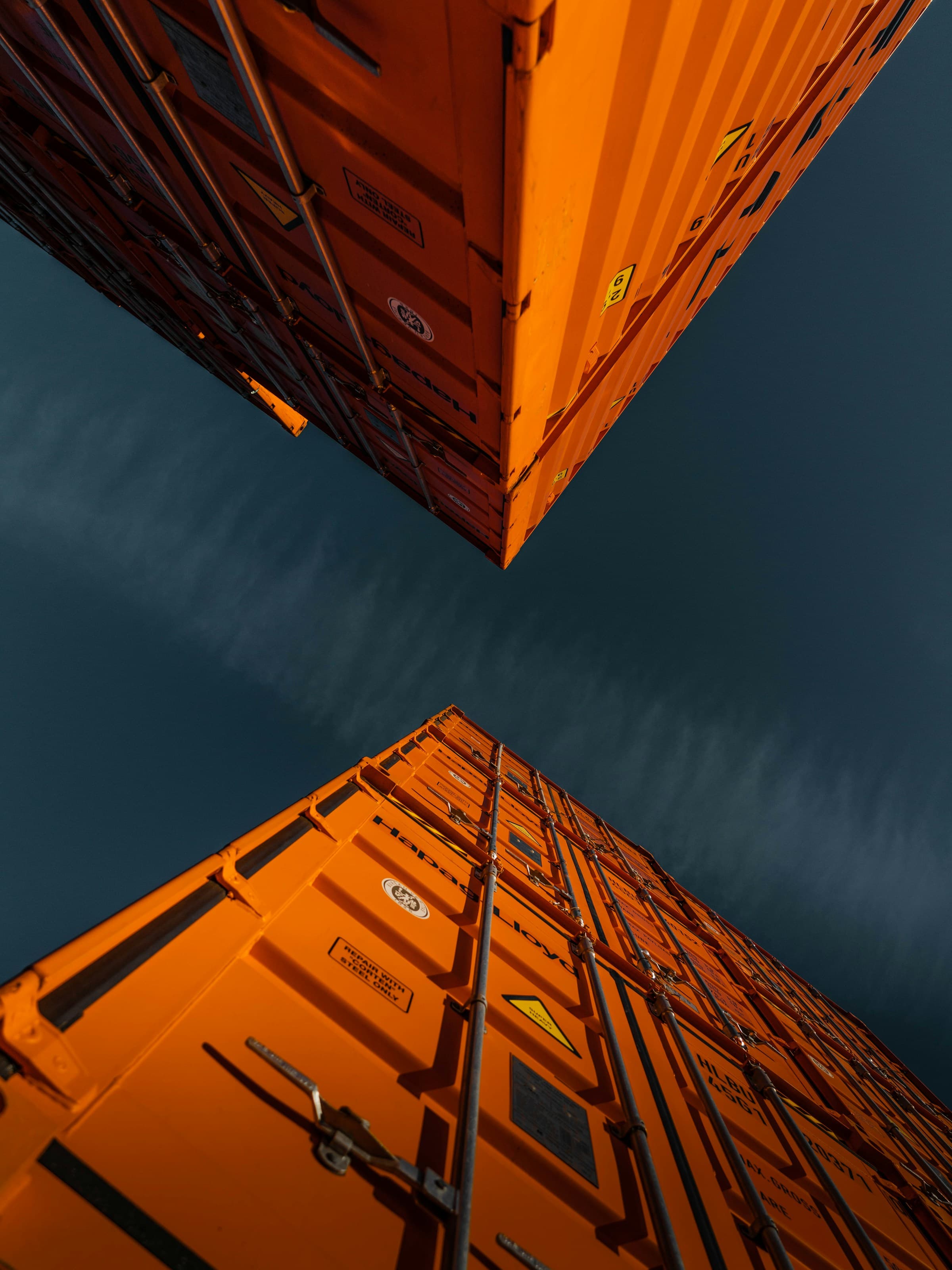 Two bright orange shipping containers stacked high, photographed from below against a dark blue sky